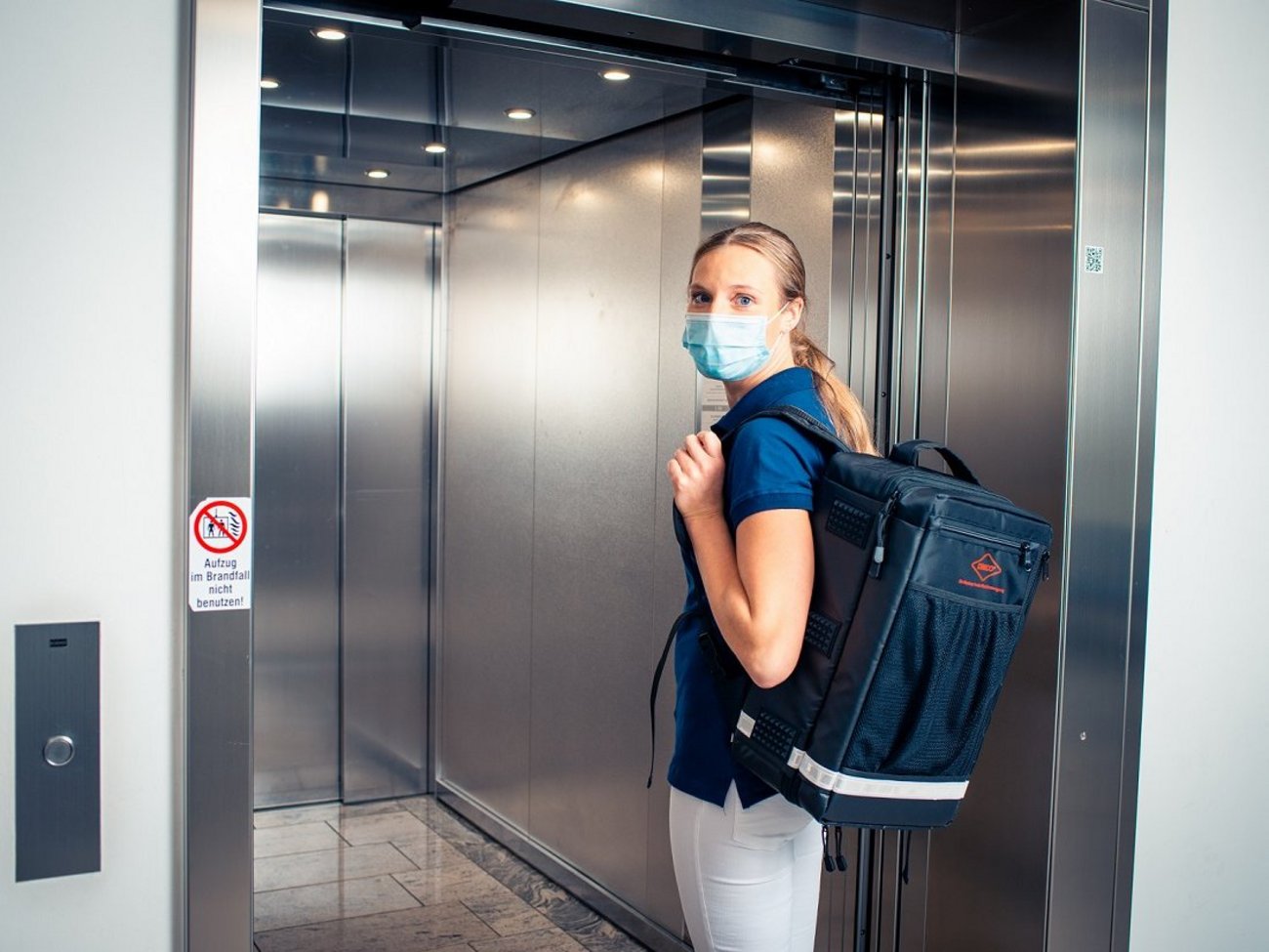 Frau mit Hausbesuchsrucksack im Einsatz im Fahrstuhl