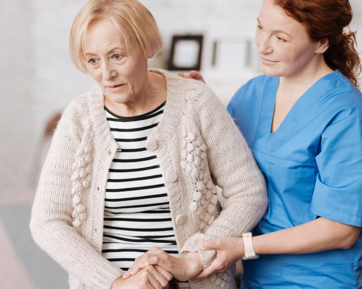 Sturzprophylaxe in der Pflege: Pflegerin assistiert Seniorin